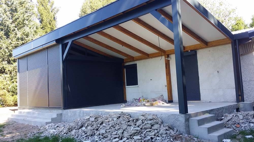 Maison partiellement construite avec toit en tôle noire, murs blancs et gravats devant.