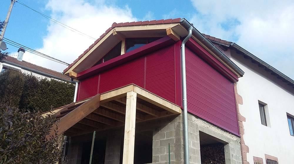 Maison à façade rouge avec porche en bois et toit en pente par une journée ensoleillée
