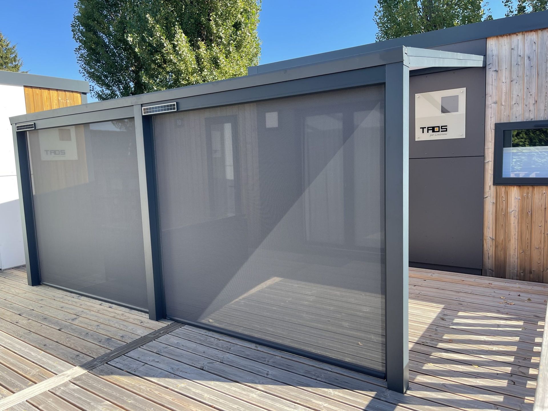 Paravent coulissant gris moderne pour préserver l'intimité sur une terrasse en bois ensoleillée à côté d'une maison