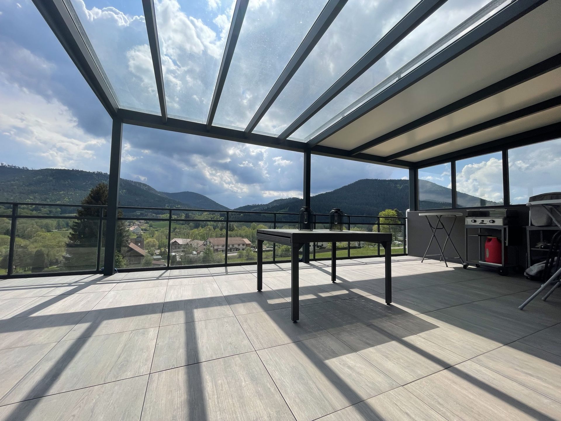 Terrasse sur le toit couverte de verre avec vue sur les montagnes au loin et une table au centre