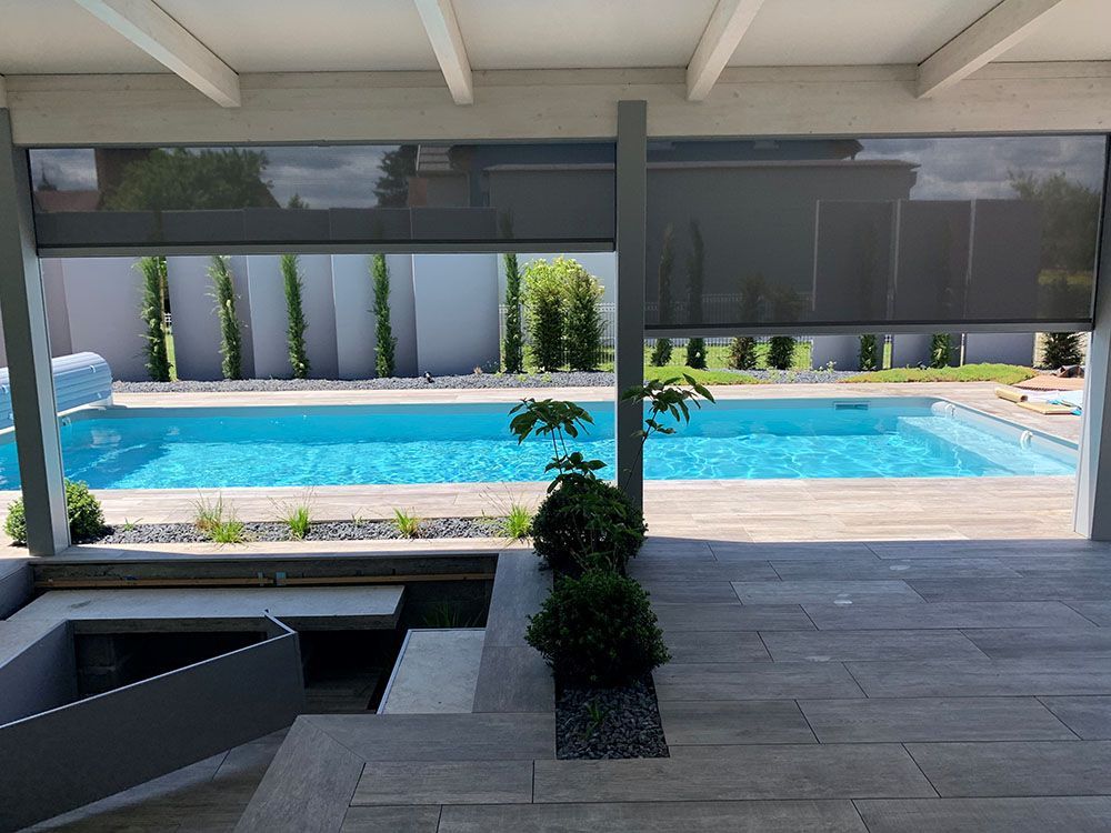 Terrasse couverte donnant sur une piscine bleu vif, agrémentée de chaises longues et de hautes haies.