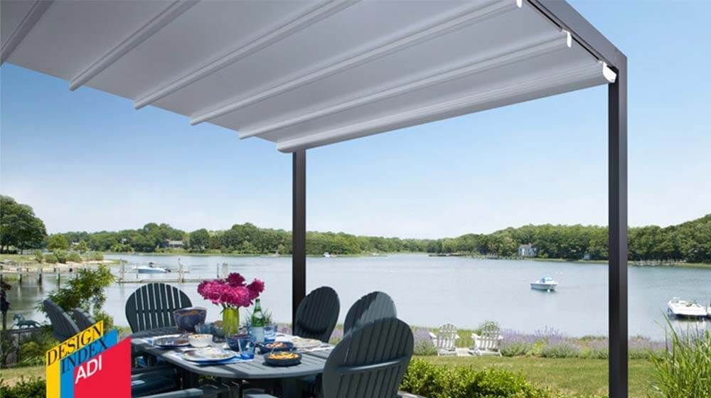 Ensemble de repas sur la terrasse sous une pergola blanche au bord d'un lac, avec des fleurs et des chaises donnant sur l'eau.