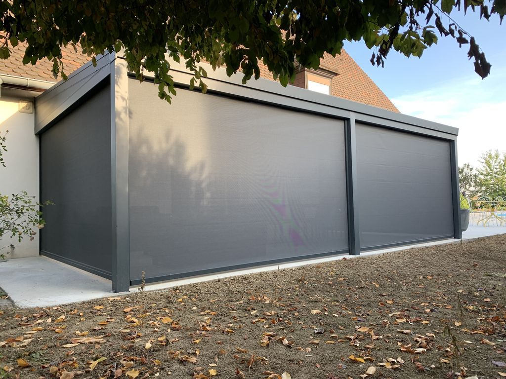 Garage gris moderne avec deux grandes portes fermées, à côté d'une allée bordée d'arbres.