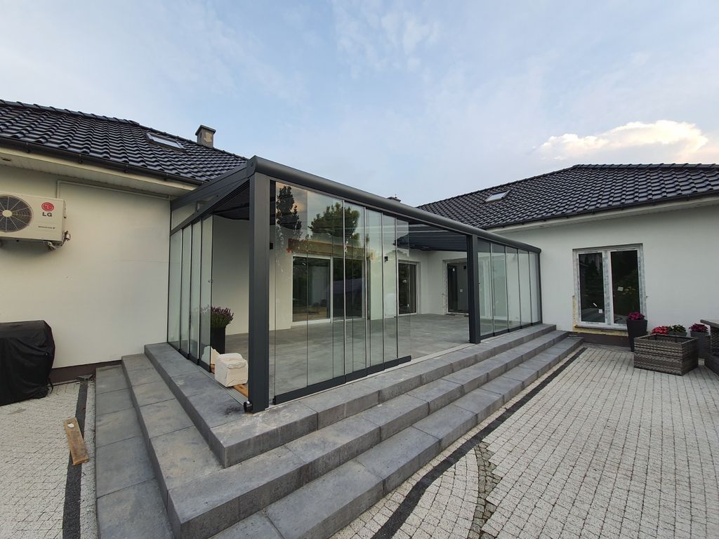 Patio de maison moderne avec extension vitrée, marches grises et cour pavée