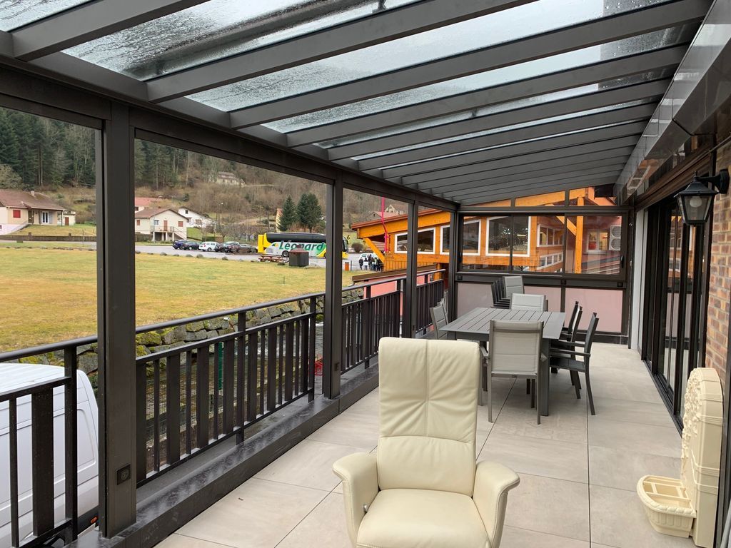 Terrasse couverte avec rambarde, chaise beige et table à manger donnant sur une cour gazonnée et des maisons.