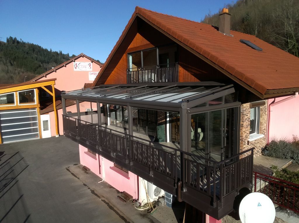 Maison au toit rouge avec balcon vitré et garage jaune, située sur un versant ensoleillé.