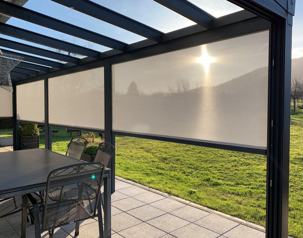 Terrasse couverte avec moustiquaires, mobilier de jardin et vue ensoleillée sur l'herbe au-delà