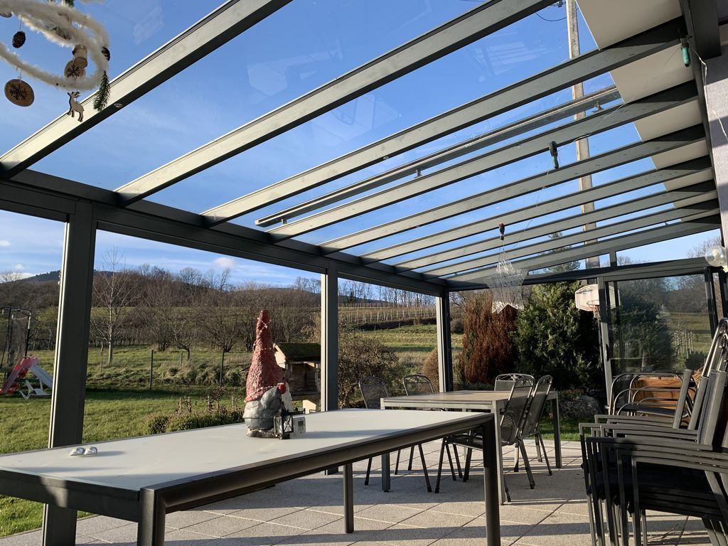 Patio avec pergola en métal, table, chaises et vue sur des champs verdoyants sous un ciel bleu