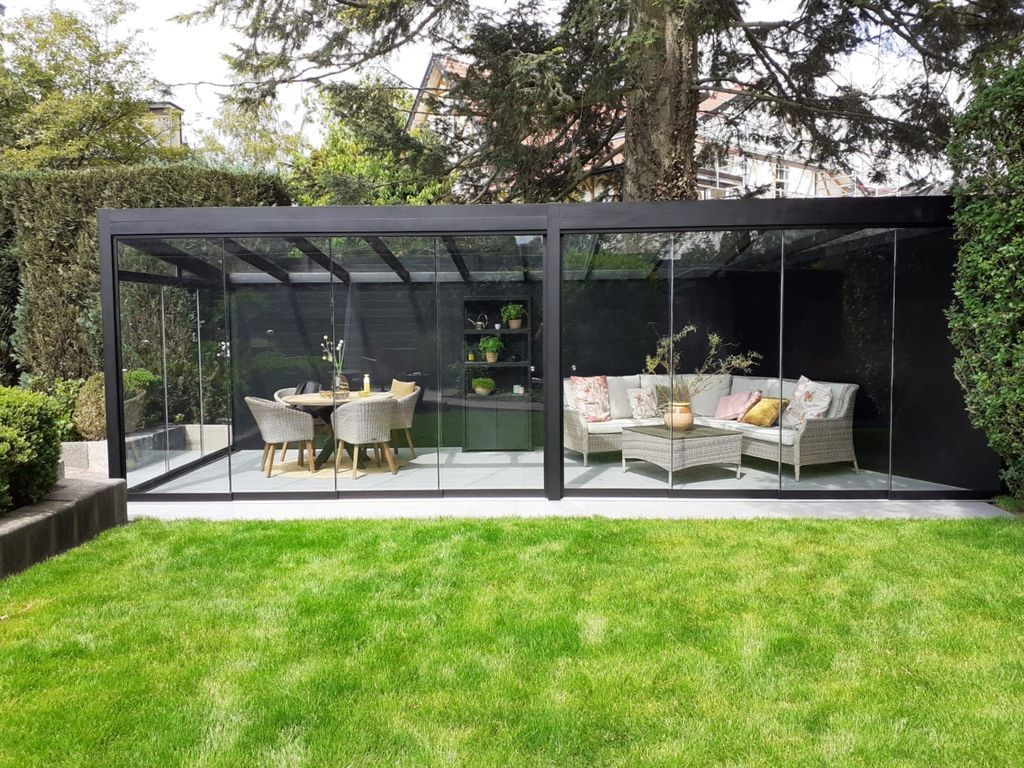 Pavillon de jardin moderne en verre avec table à manger et salon de jardin donnant sur une pelouse verdoyante