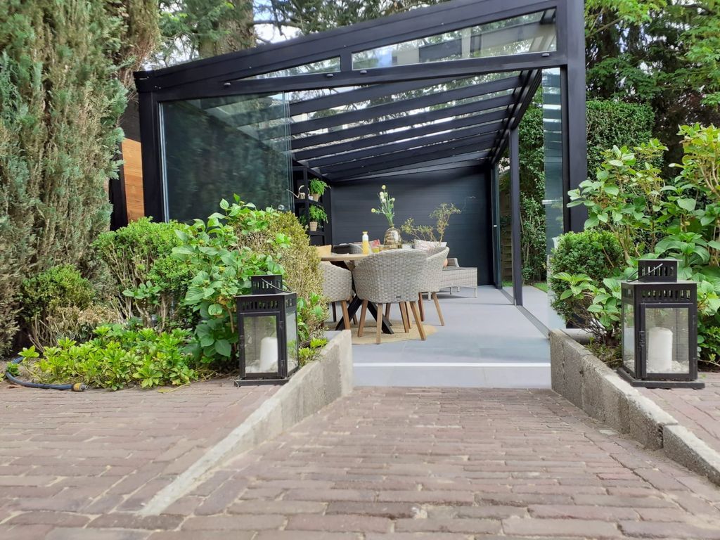 Allée moderne menant à un espace repas extérieur couvert, agrémenté de verdure et de lanternes.
