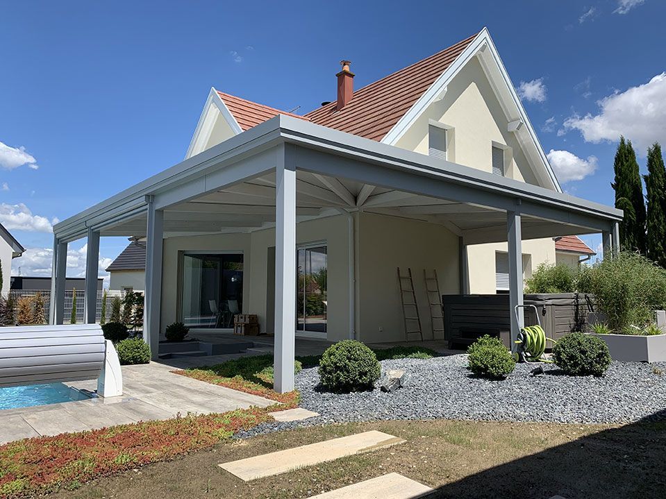 Maison blanche moderne avec patio couvert, toit de tuiles rouges et jardin paysager à l'avant sous un ciel bleu