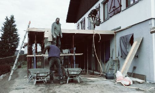 Deux ouvriers sur un échafaudage à l'extérieur d'une maison, effectuant des travaux de construction extérieure.