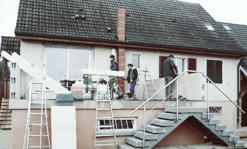 Des personnes sur la terrasse d'une maison avec escalier, rambarde et toit en pente en arrière-plan
