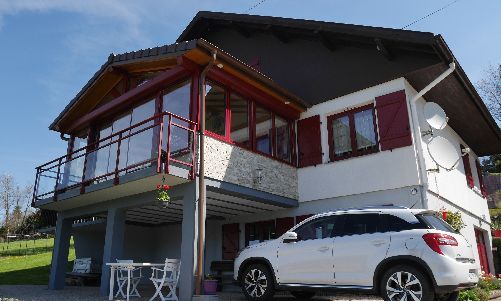 Maison à deux étages avec balcon aux bordures rouges et un SUV blanc garé en dessous