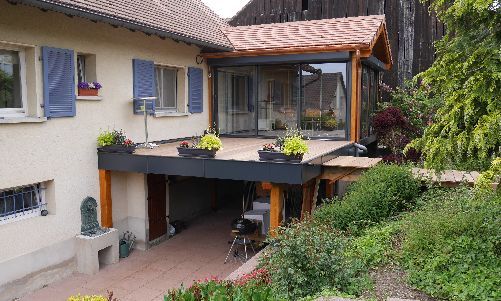 Maison d'habitation avec patio couvert et balcon à l'étage, entourée d'arbres et de verdure.