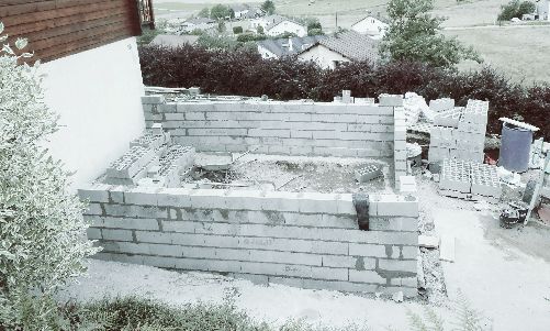 Petit bac à jardin en briques d'extérieur ou plate-bande surélevée à côté d'un mur blanc et d'une clôture en bois.