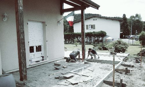 Dégâts sur la terrasse d'une maison après une tempête : des débris et des ouvriers dégagent les gravats près d'un bâtiment blanc.
