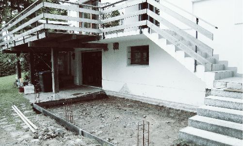 Extérieur d'une maison blanche avec un escalier surélevé et un fossé de terre au premier plan