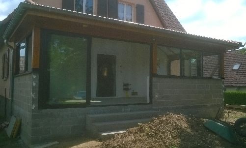 Maison moderne avec façade en bois, grandes fenêtres, porte d'entrée et jardin non aménagé.