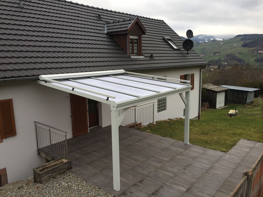 Patio de maison avec un auvent blanc de style pergola au-dessus d'une terrasse carrelée, donnant sur une cour gazonnée et des collines.
