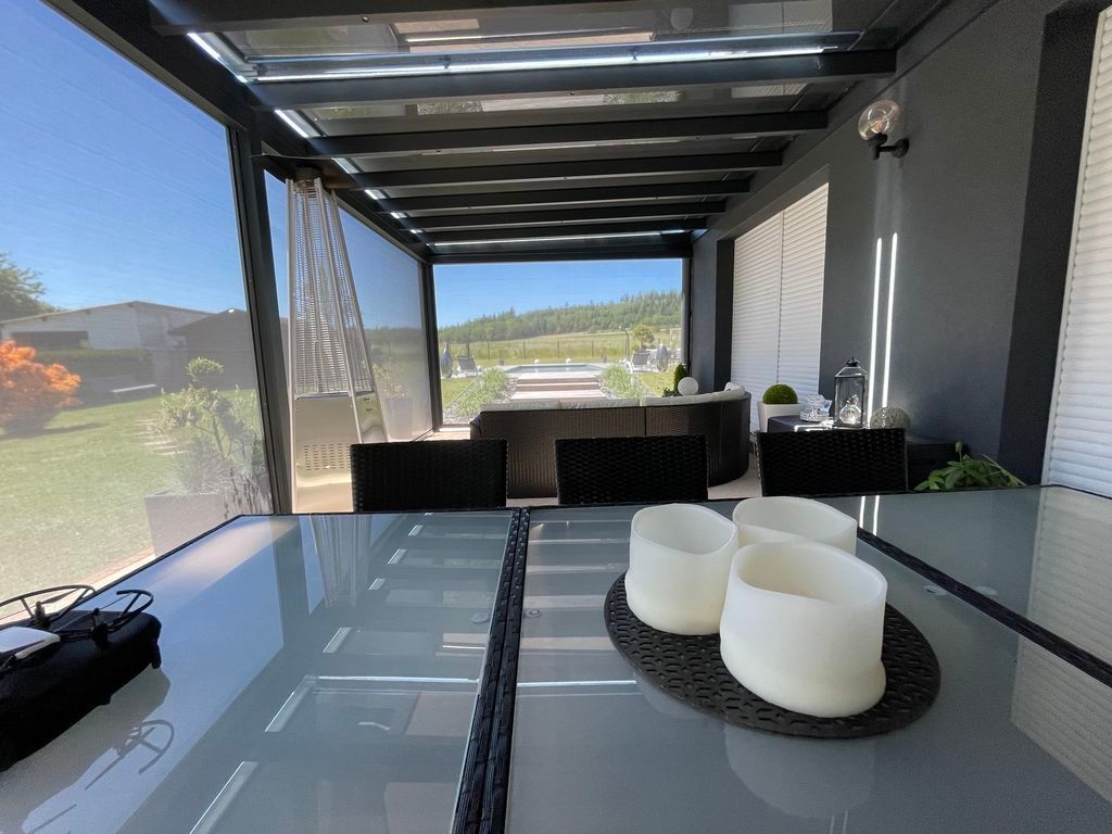 Terrasse couverte avec coin repas, table en verre, bougies blanches, chaises noires et vue sur le lac.