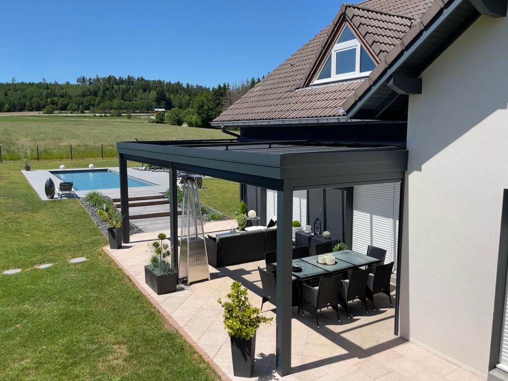 Patio d'une maison moderne avec pergola noire, table à manger, plantes en pot et jardin gazonné près d'une piscine