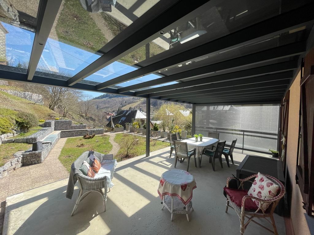 Terrasse couverte avec sièges, toit en puits de lumière et personnes se détendant dans un jardin ensoleillé à l'arrière.