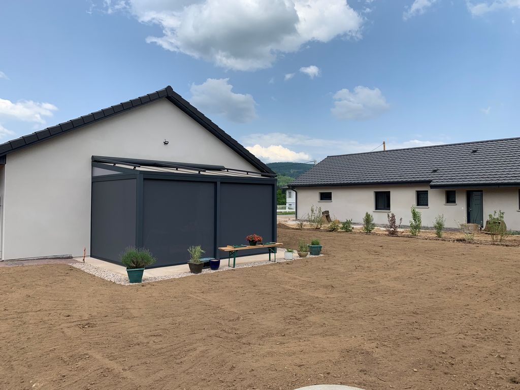 Maison blanche moderne avec toit foncé et patio clôturé dans un jardin nouvellement aménagé sous un ciel nuageux