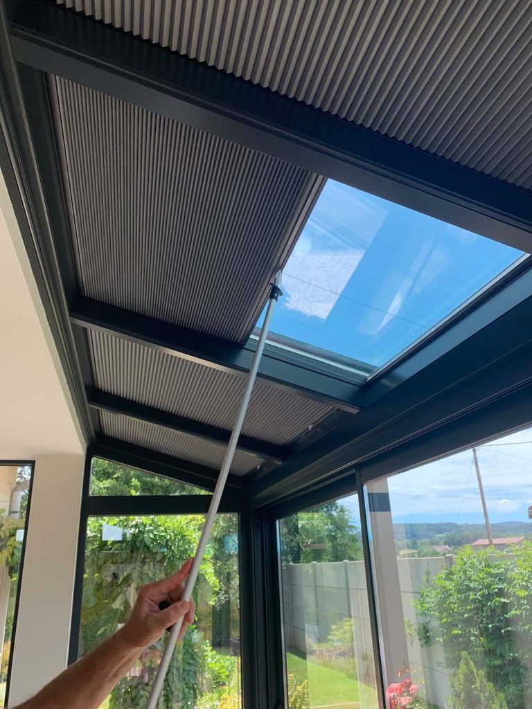 Main tenant une perche ouvrant un puits de lumière dans une véranda moderne au toit de verre