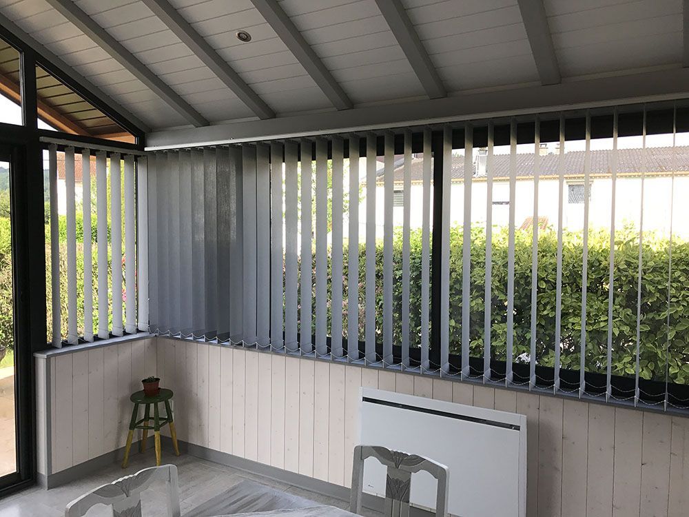 Terrasse couverte avec stores verticaux, un tabouret et un petit radiateur adossé au mur.
