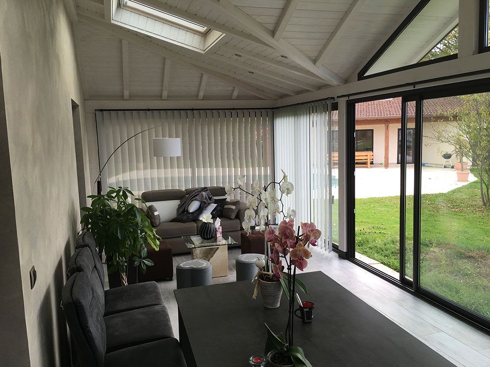 Patio couvert moderne avec table à manger noire, canapé, plantes en pot et grandes portes vitrées donnant sur un jardin