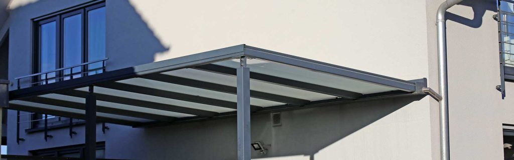 Auvent bleu avec supports métalliques fixé à un extérieur de bâtiment beige