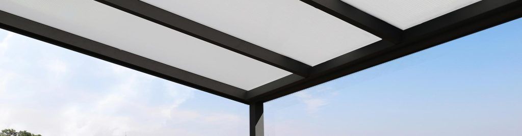 La structure en métal noir de la pergola de terrasse se détache sur un ciel bleu partiellement nuageux.