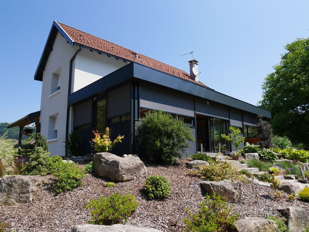 Maison moderne avec toit rouge en pente et jardin paysager par une journée ensoleillée