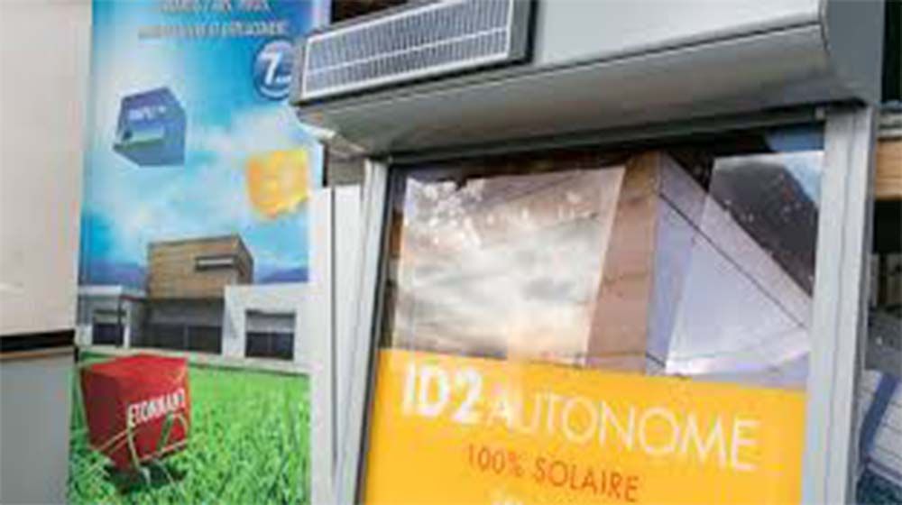 Kiosque solaire avec enseigne orange 1D2 AUTONOME et panneau solaire intégré à une vitrine.