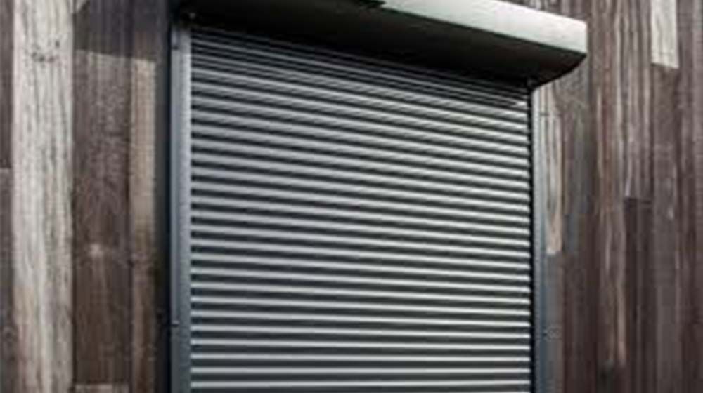 Volet roulant métallique gris fermé sur un mur extérieur en bois