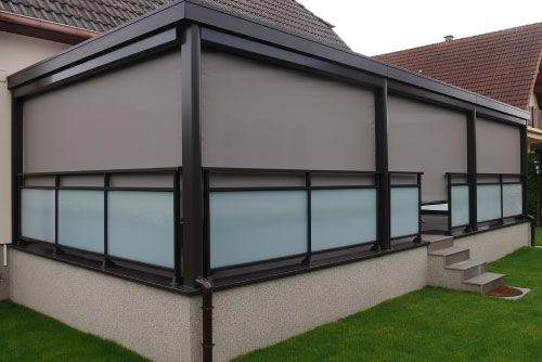 Maison moderne avec patio vitré et finitions foncées dans un jardin gazonné