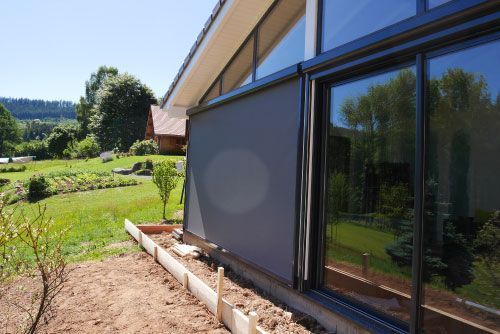 Extérieur d'une maison moderne avec de grandes fenêtres donnant sur une cour et un jardin gazonnés par une journée ensoleillée