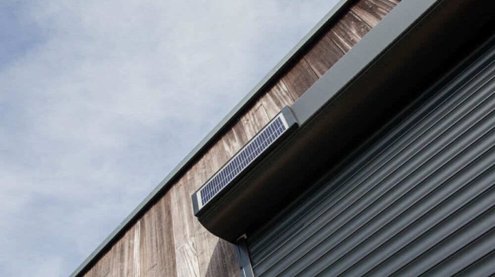 Gros plan sur un coin de bâtiment avec un auvent métallique sombre se détachant sur un ciel nuageux.