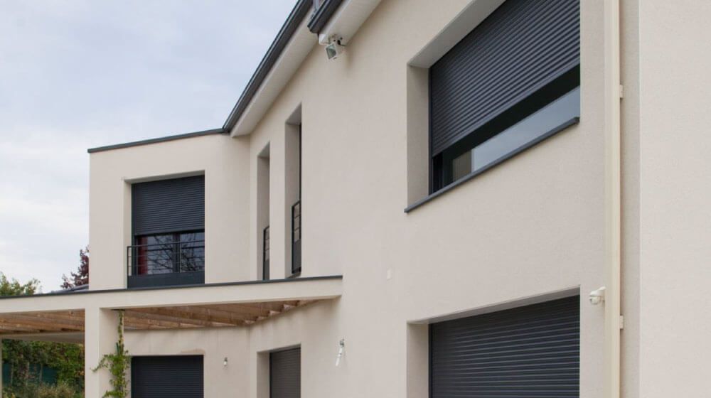 Maison moderne beige de deux étages avec volets roulants foncés et balcon