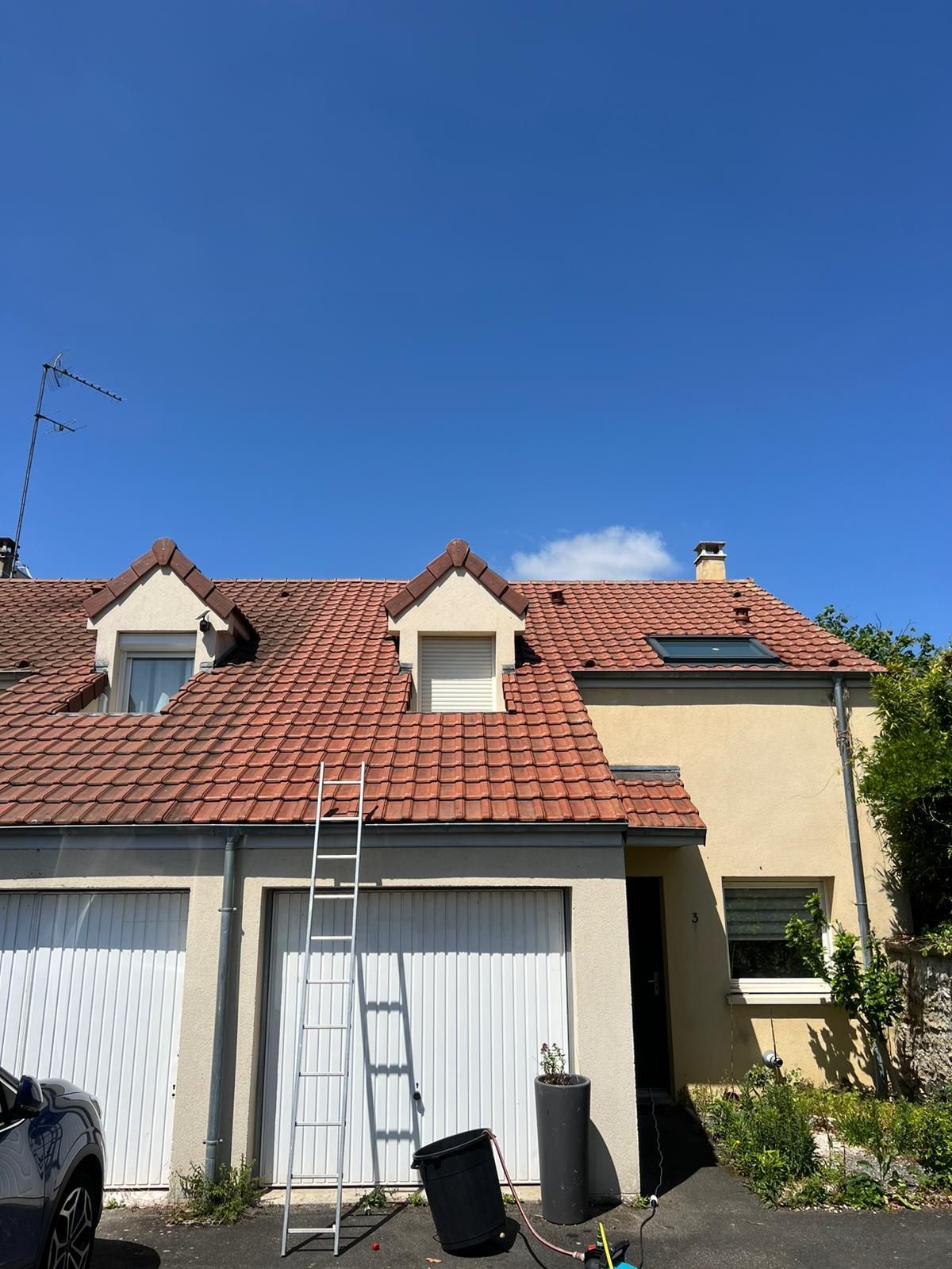 Nettoyage à haute pression d'un toit recouvert de mousse, révélant des tuiles orange propres.