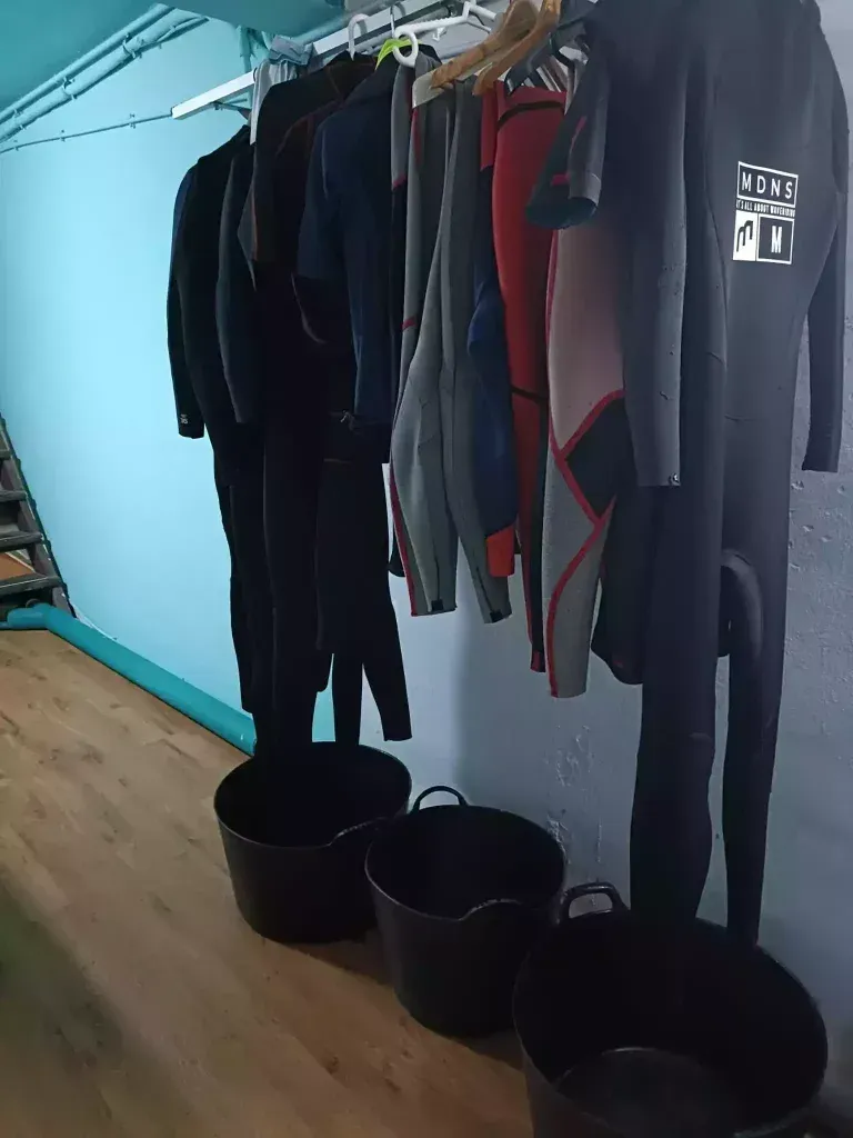 Un montón de trajes de neopreno están colgados en un estante en una habitación.