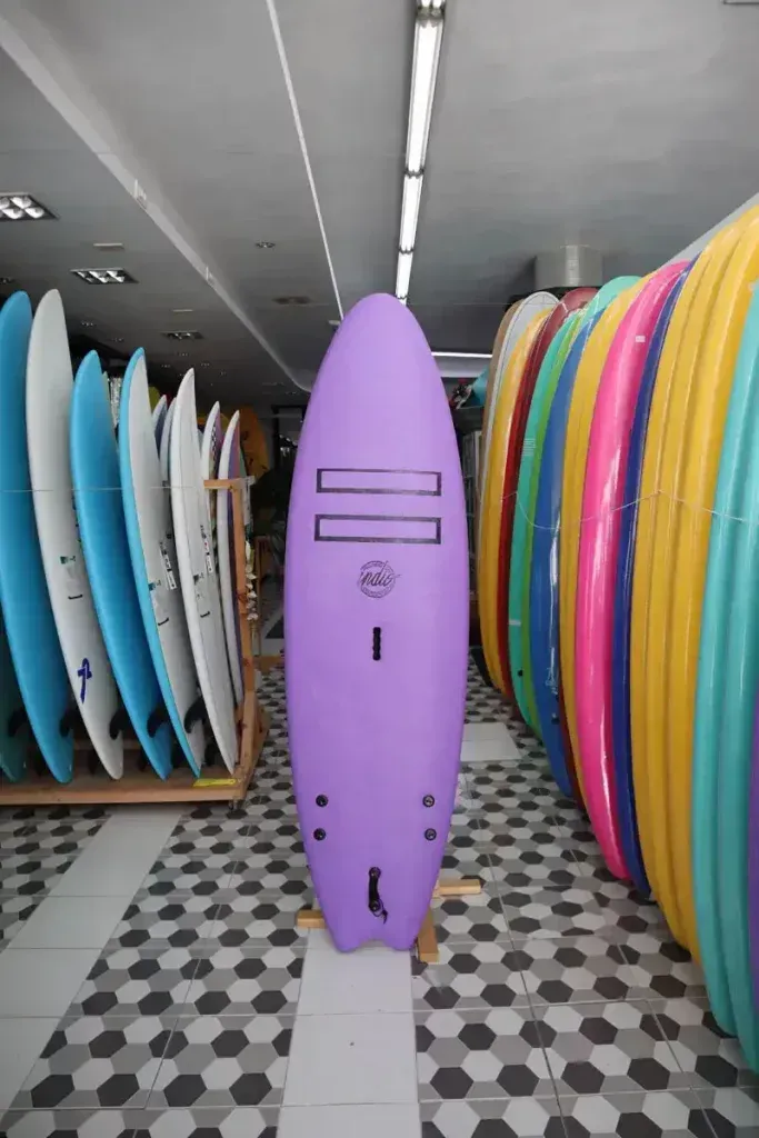 Una tabla de surf morada en una tienda rodeada de otras tablas de surf.