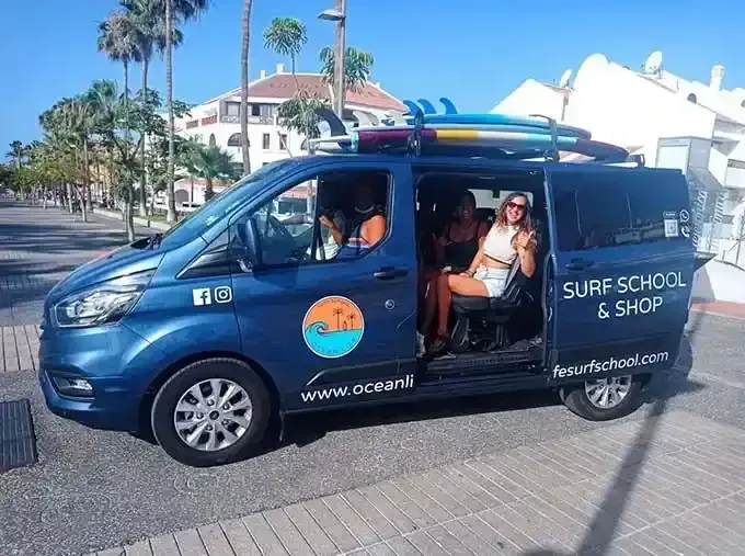 Una camioneta azul con tablas de surf encima está estacionada al costado de la carretera.