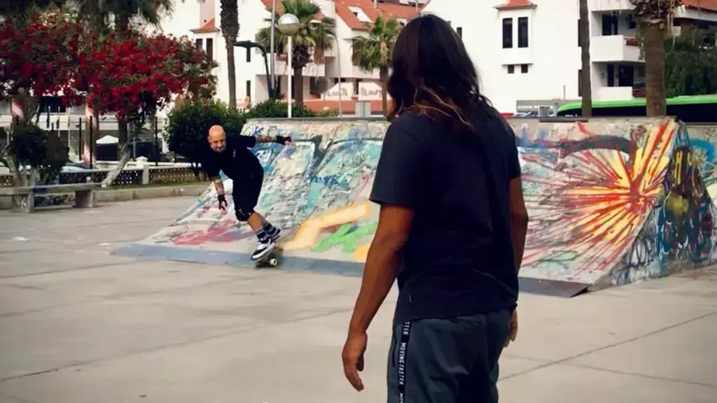 Un hombre de pie junto a un patinador en un parque de patinaje.