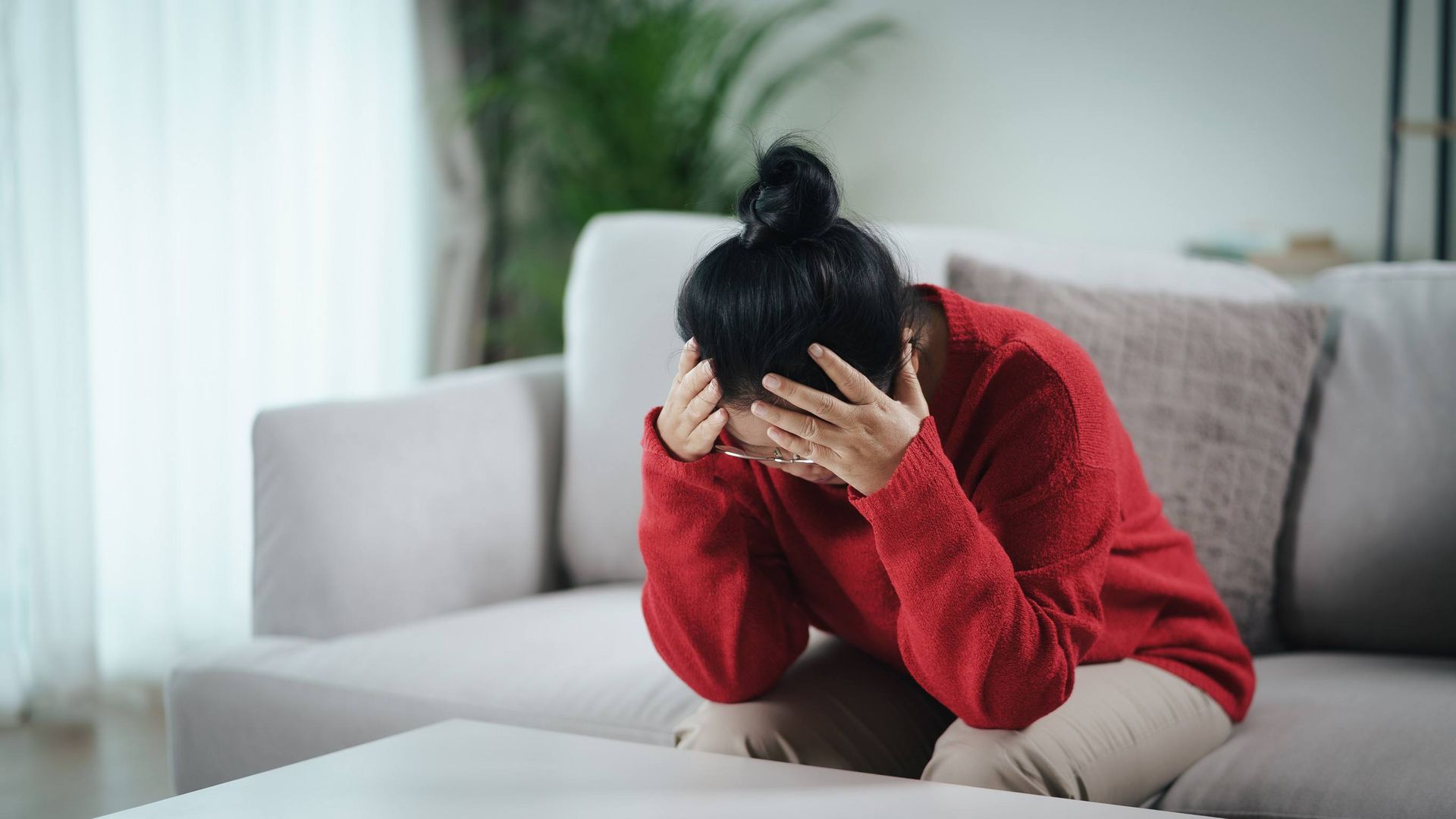 Una mujer está sentada en un sofá con la cabeza entre las manos.