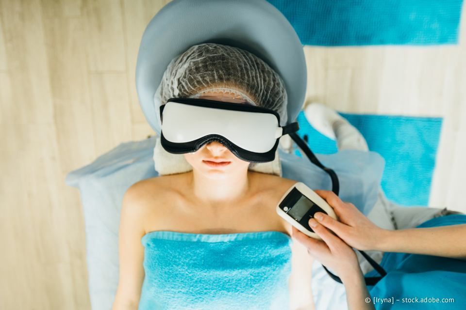 Person bei einer Spa-Behandlung, trägt Augenmaske und Haarnetz und wird mit einem Gerät behandelt, blaues Handtuch.