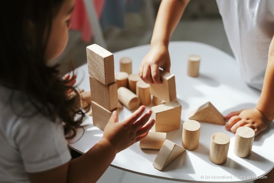 Zwei Kinder bauen mit Holzklötzen auf einem weißen Tisch.