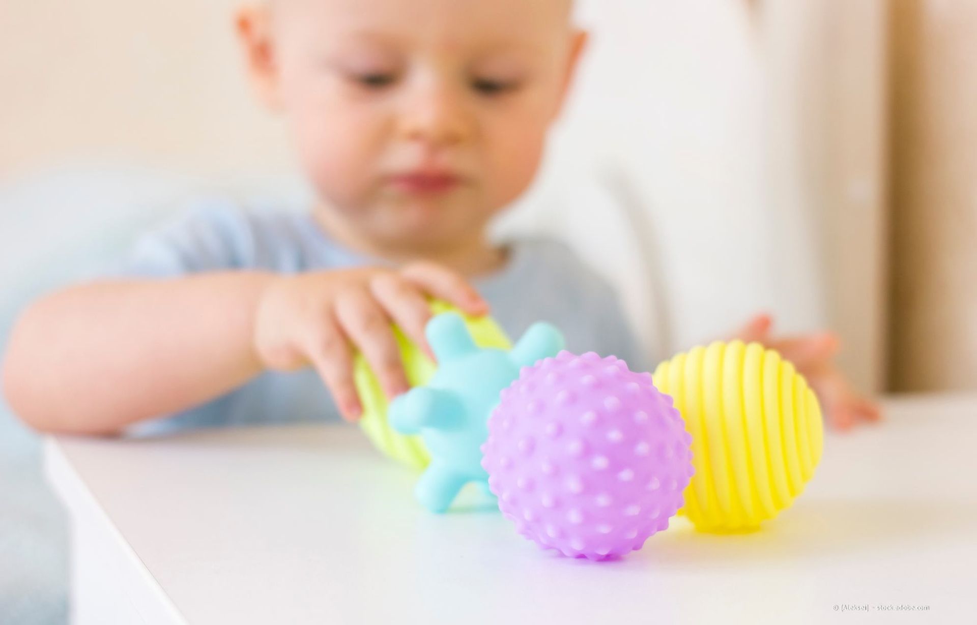 Baby spielt mit strukturierten, bunten Sinnesbällen auf einem weißen Tisch.