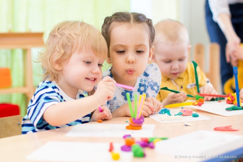 Kinder sitzen an einem Tisch und formen bunte Tonfiguren in einer Klassenzimmerumgebung.
